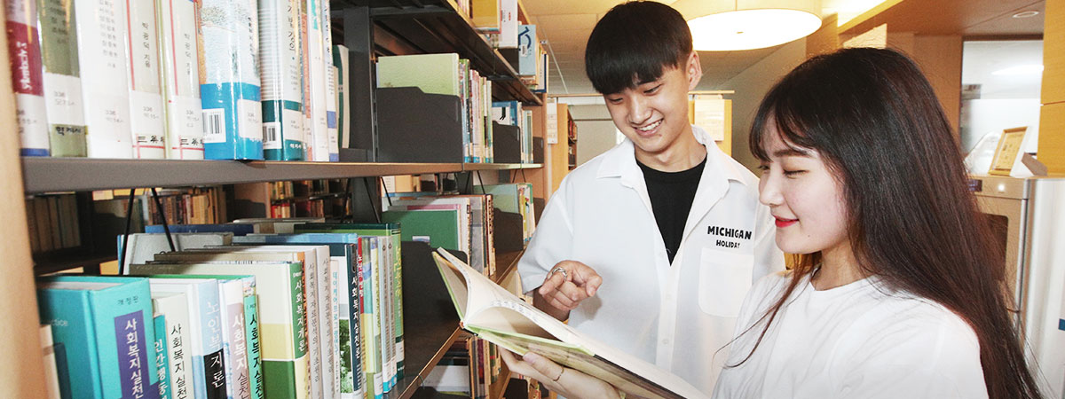 도서관에서 두 학생이 함게 책을 읽으며 학습하는 사진