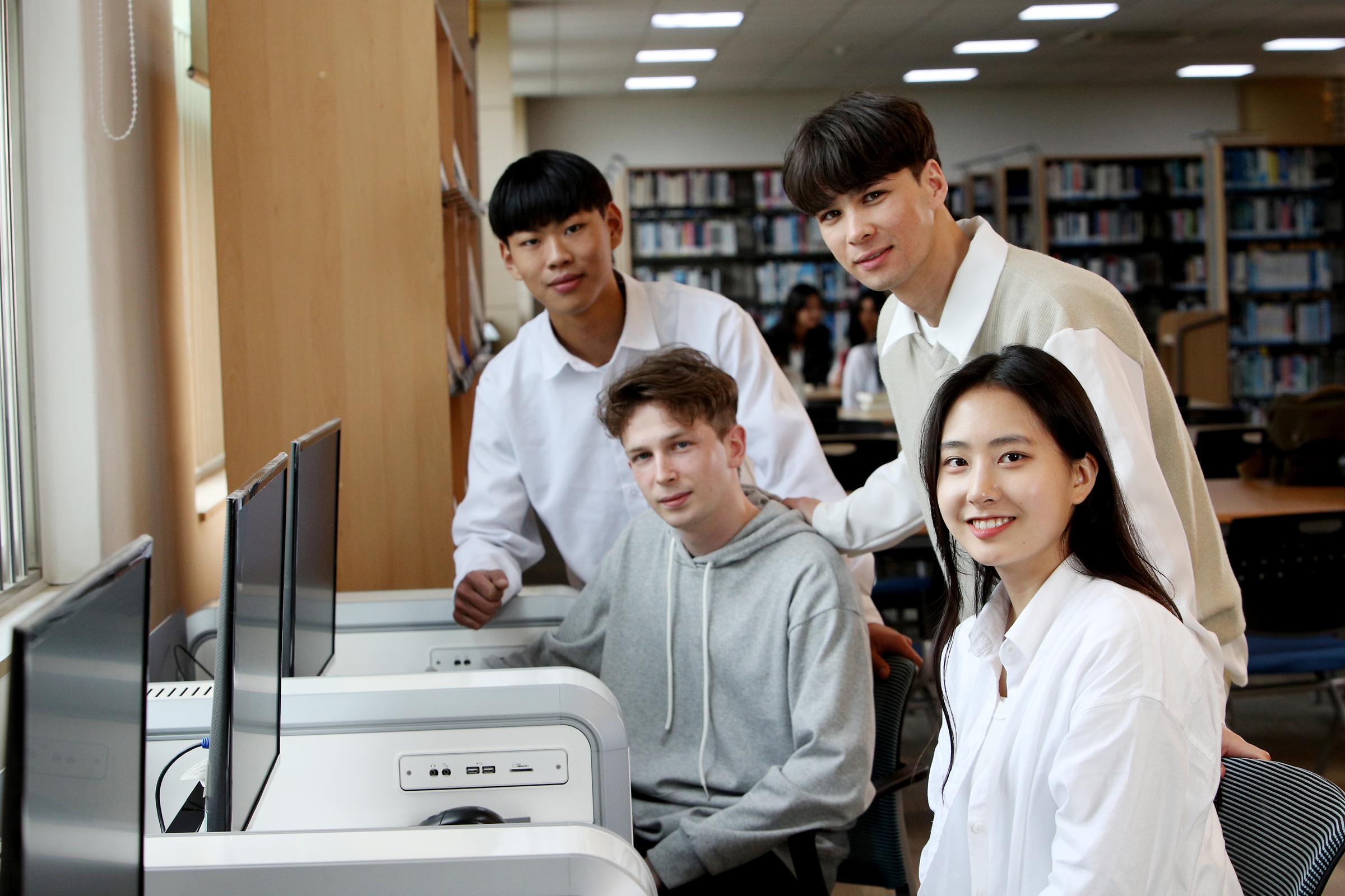 도서관의 컴퓨터 앞에 앉아 이야기를 나누는 네 명의 학생들 사진