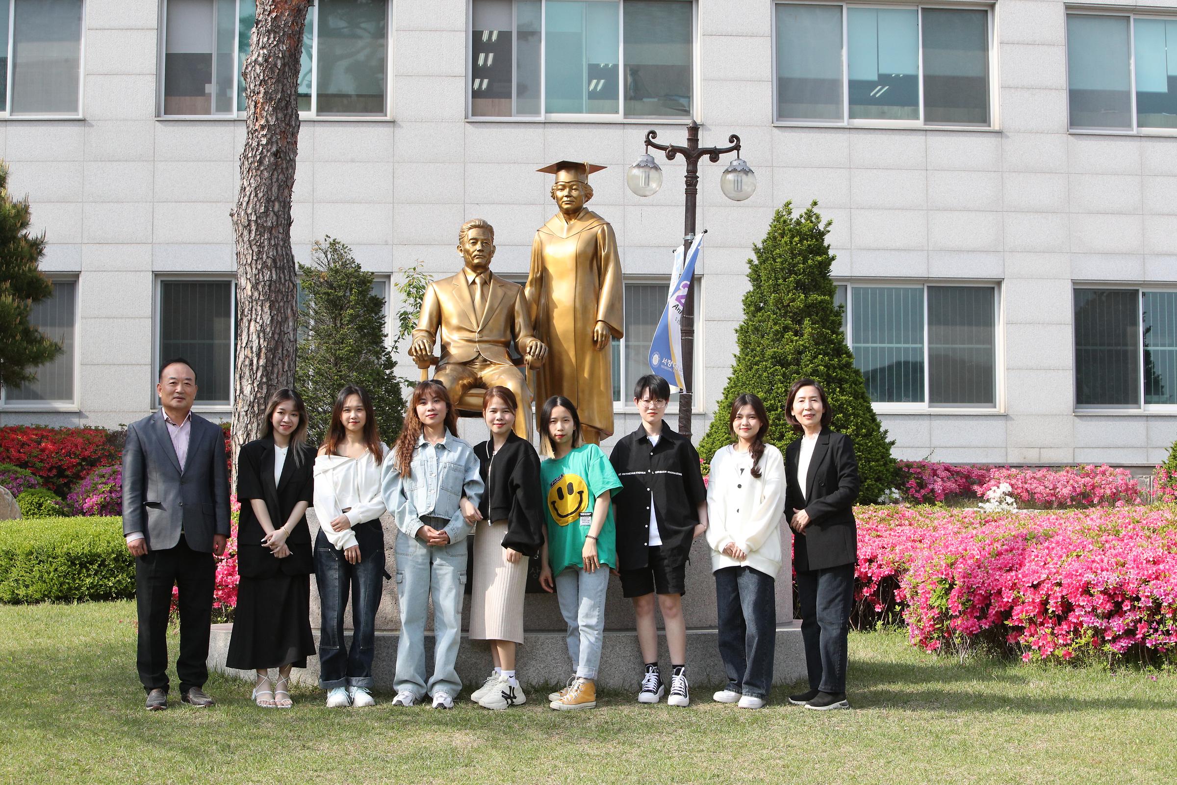 금색 인물 동상 앞에 서 있는 의료코디네이션 학과 학생들과 교수님