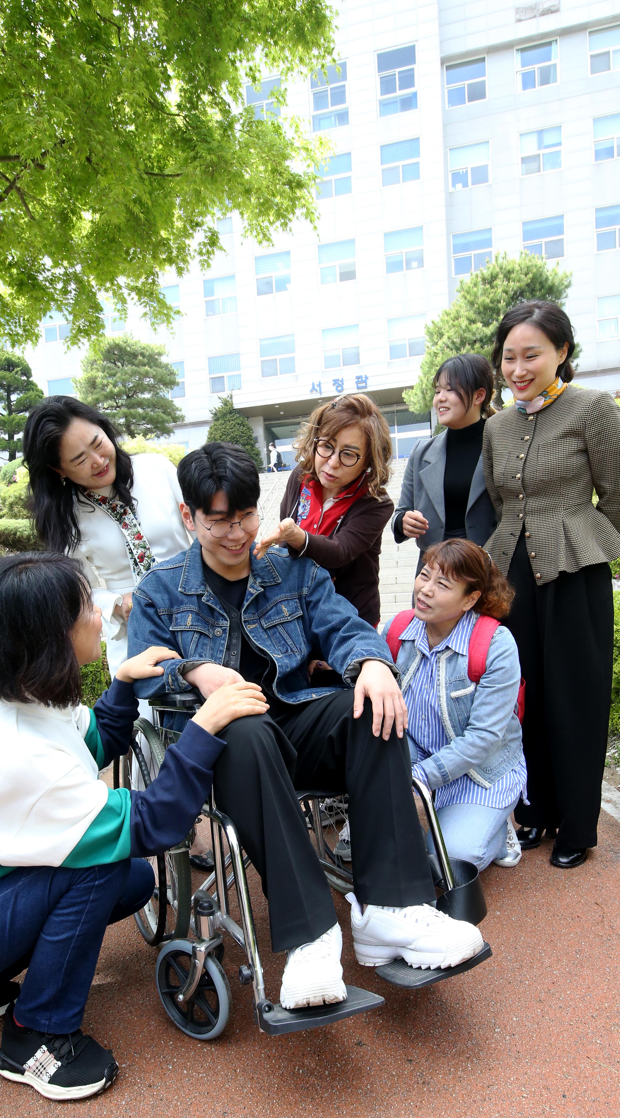 서정관 정문 앞 정자를 배경으로 화단에 앉아 찍은 사회복지과 사진. 다양한 연령의 학생들과 교수님 여러명(20명 이상)이 모여 저마다 하트 포즈를 하고있다.